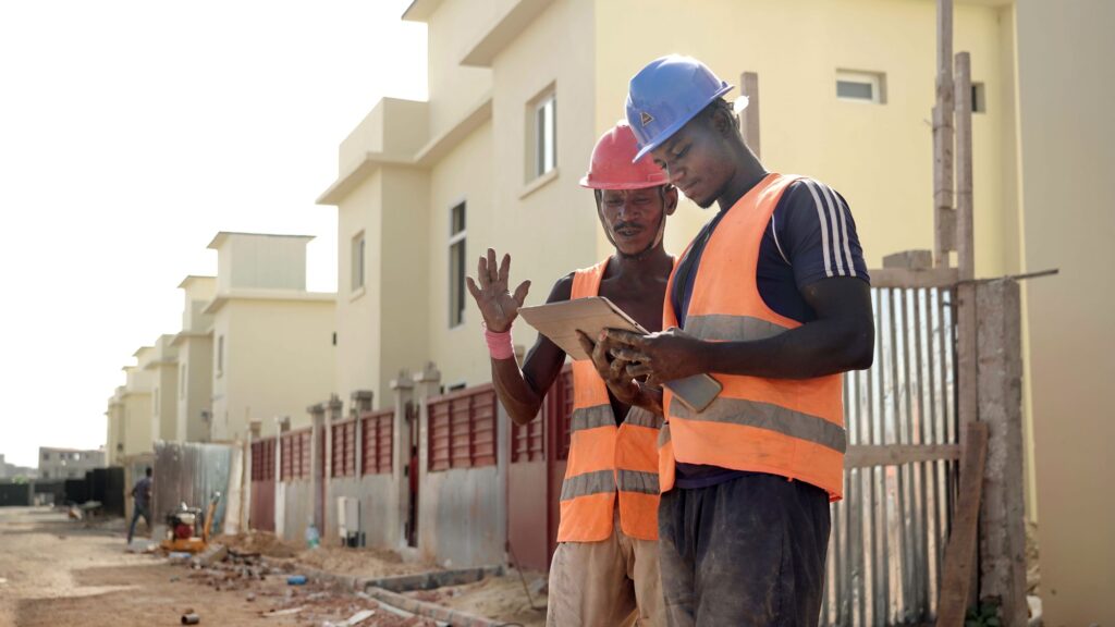 Two workers in high-visibility vests studying a tablet at a street construction site