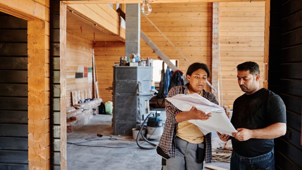A worker holding a rolled drawing inside a timber-lined building being fitted out
