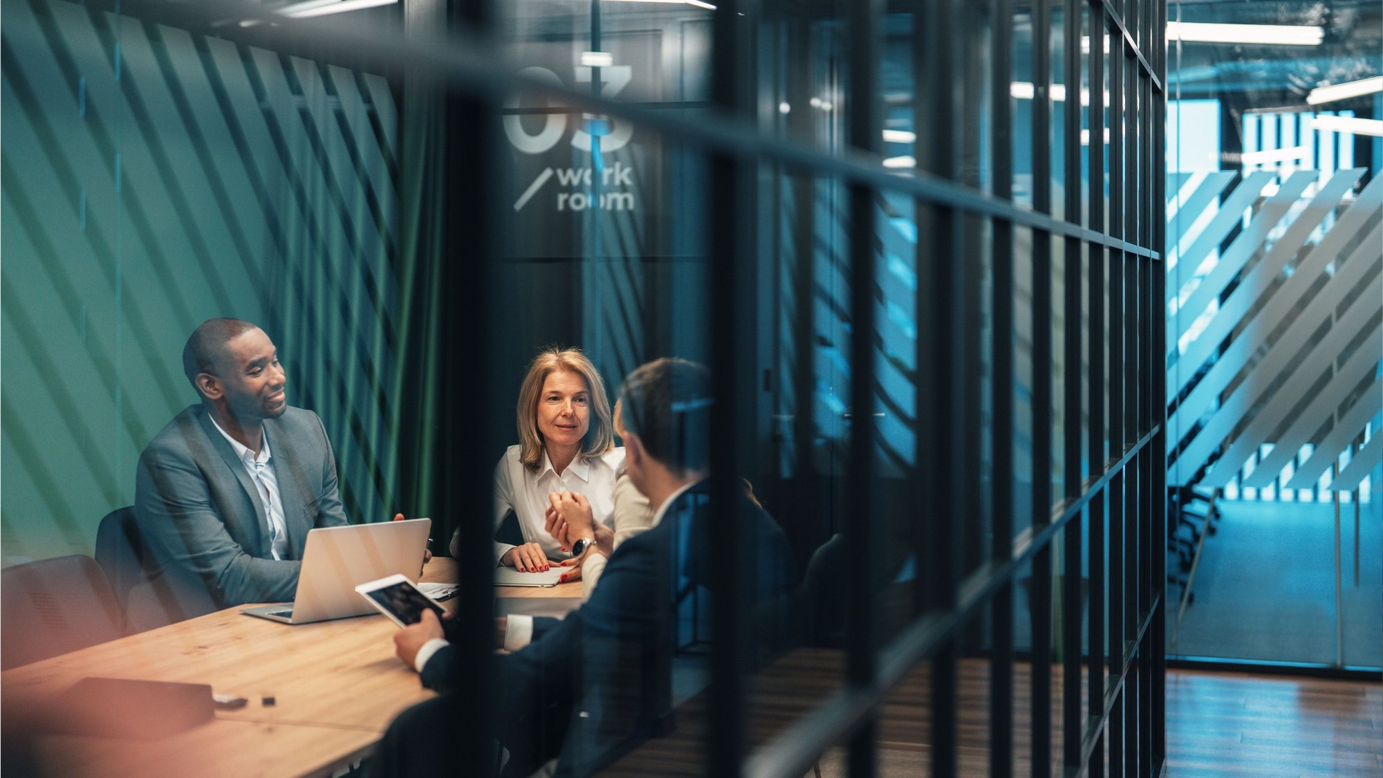 Four colleagues meeting around a table in a glass-walled meeting room