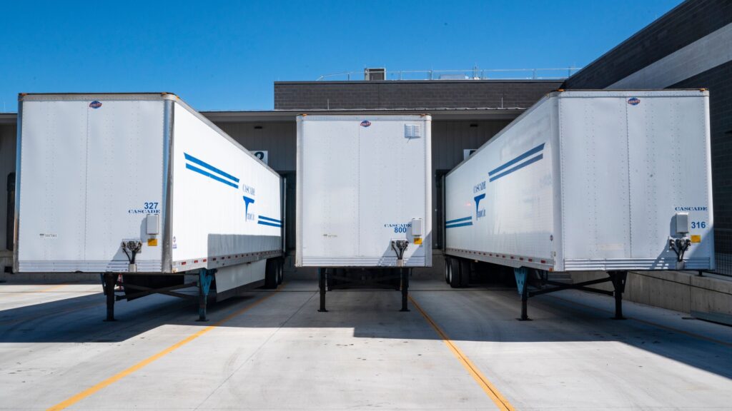 Three white trailers backed up to the doors of a distribution warehouse