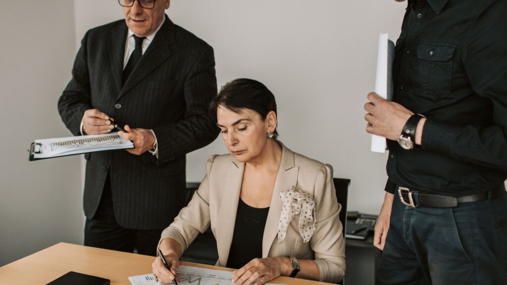 Three colleagues in business dress reviewing printed documents together at a desk