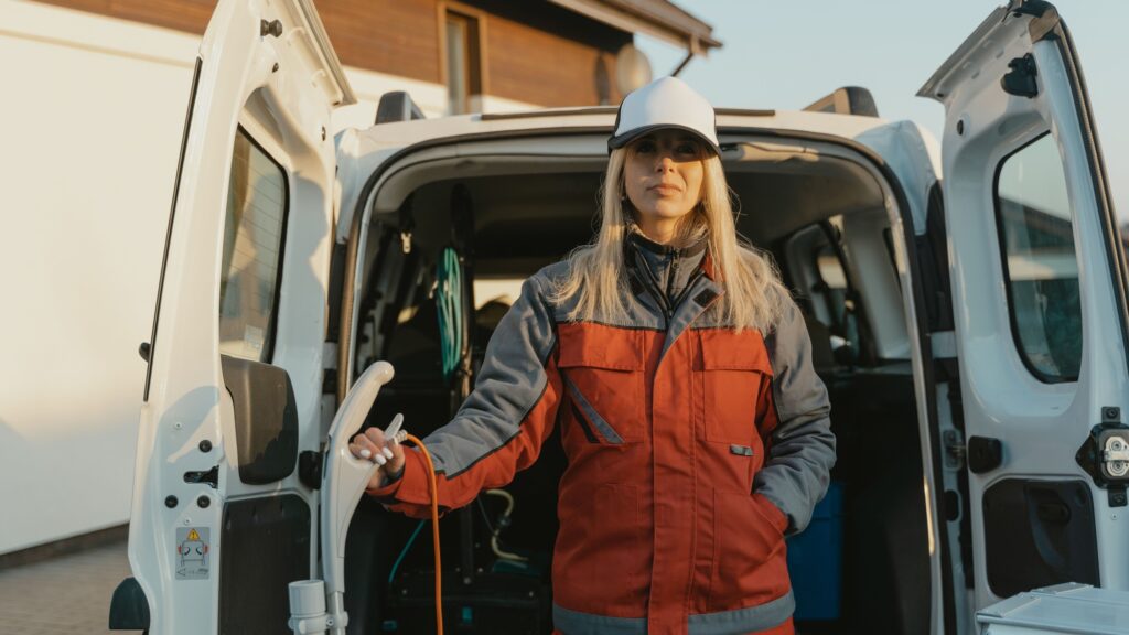 A worker in a hard hat and insulated jacket standing at the open rear doors of a service van