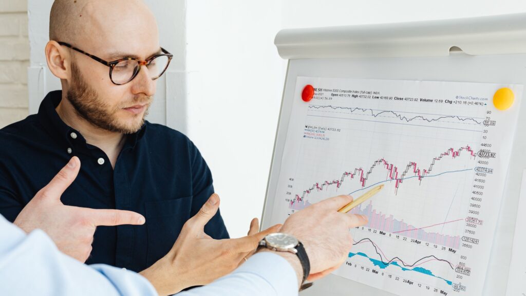 Two colleagues at a flip chart marked with line graphs, one pointing at the trend