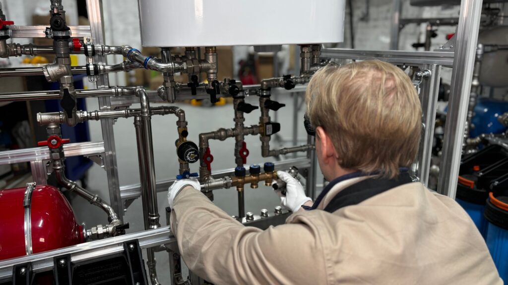 A technician adjusting valves on a wall-mounted heating manifold of copper pipework