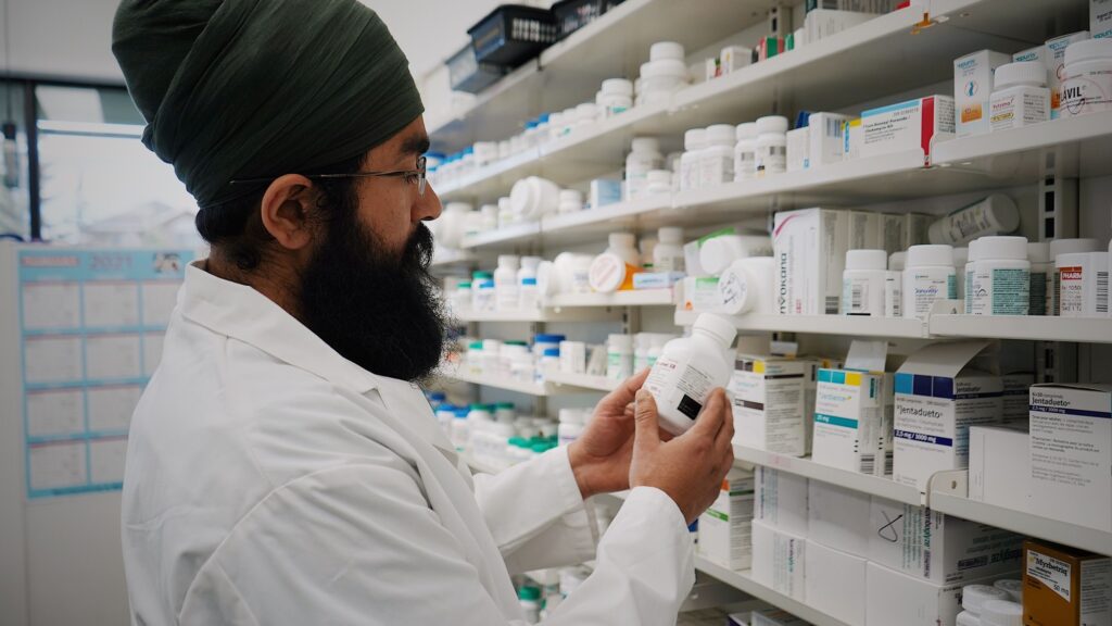 A pharmacist checking a box against the stock on a wall of pharmacy shelves