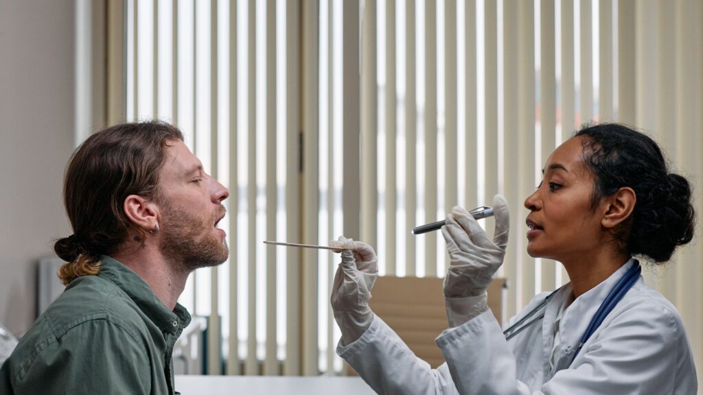 A clinician in gloves examining a patient’s throat with a tongue depressor