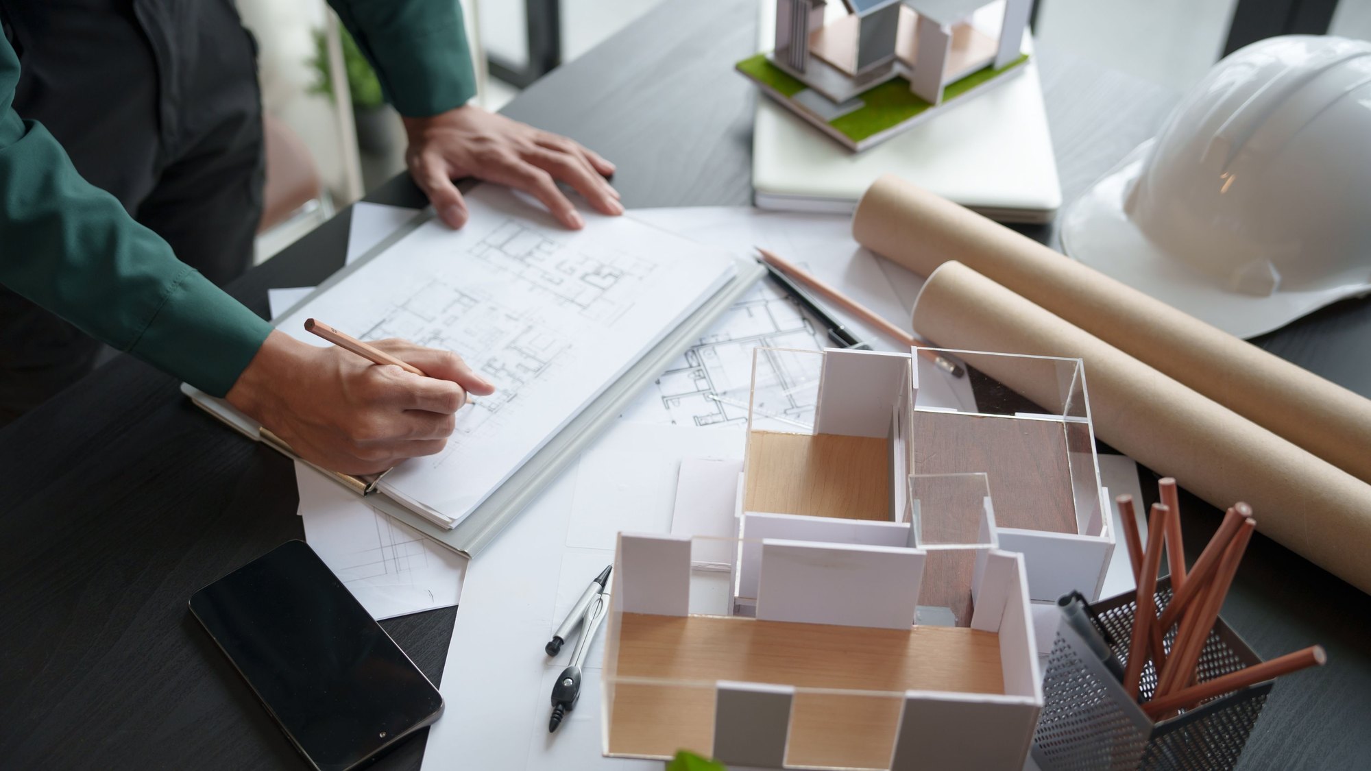 Hands sketching on drawings beside a white card architectural model of a building
