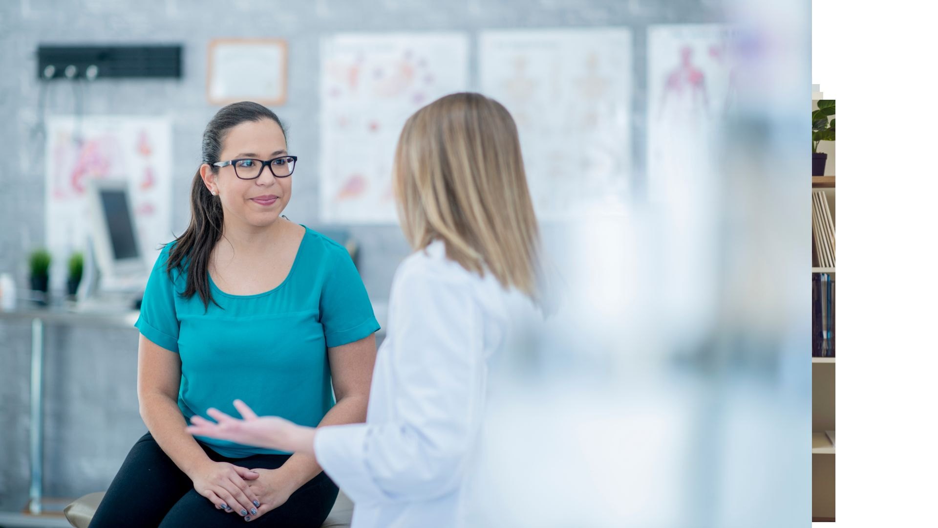 Two women talking in a consulting room hung with anatomical charts