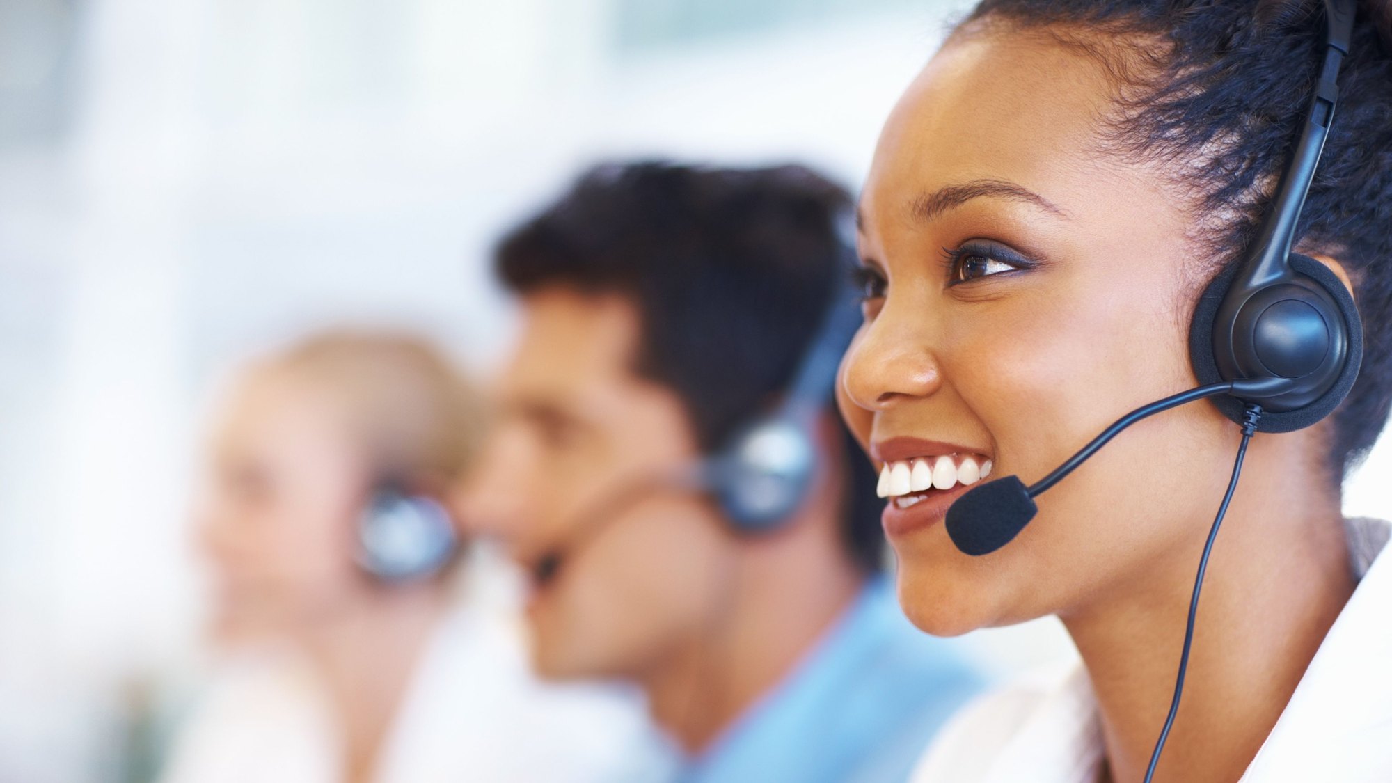 A row of call centre agents wearing headsets, the nearest one smiling