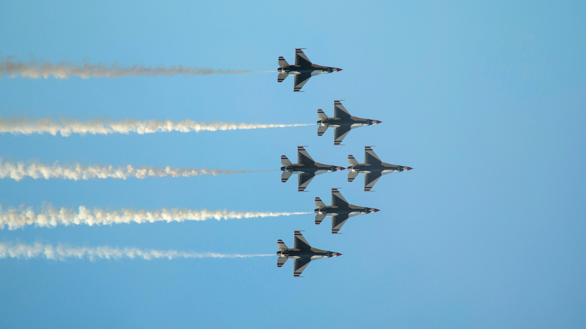 Five fighter jets flying in formation, smoke trailing behind them against a blue sky