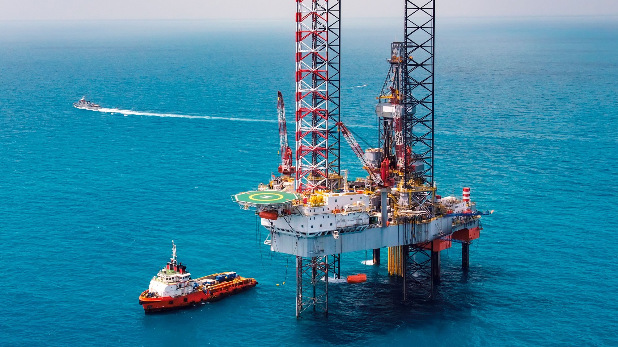 An offshore drilling rig in turquoise open water with a supply vessel alongside