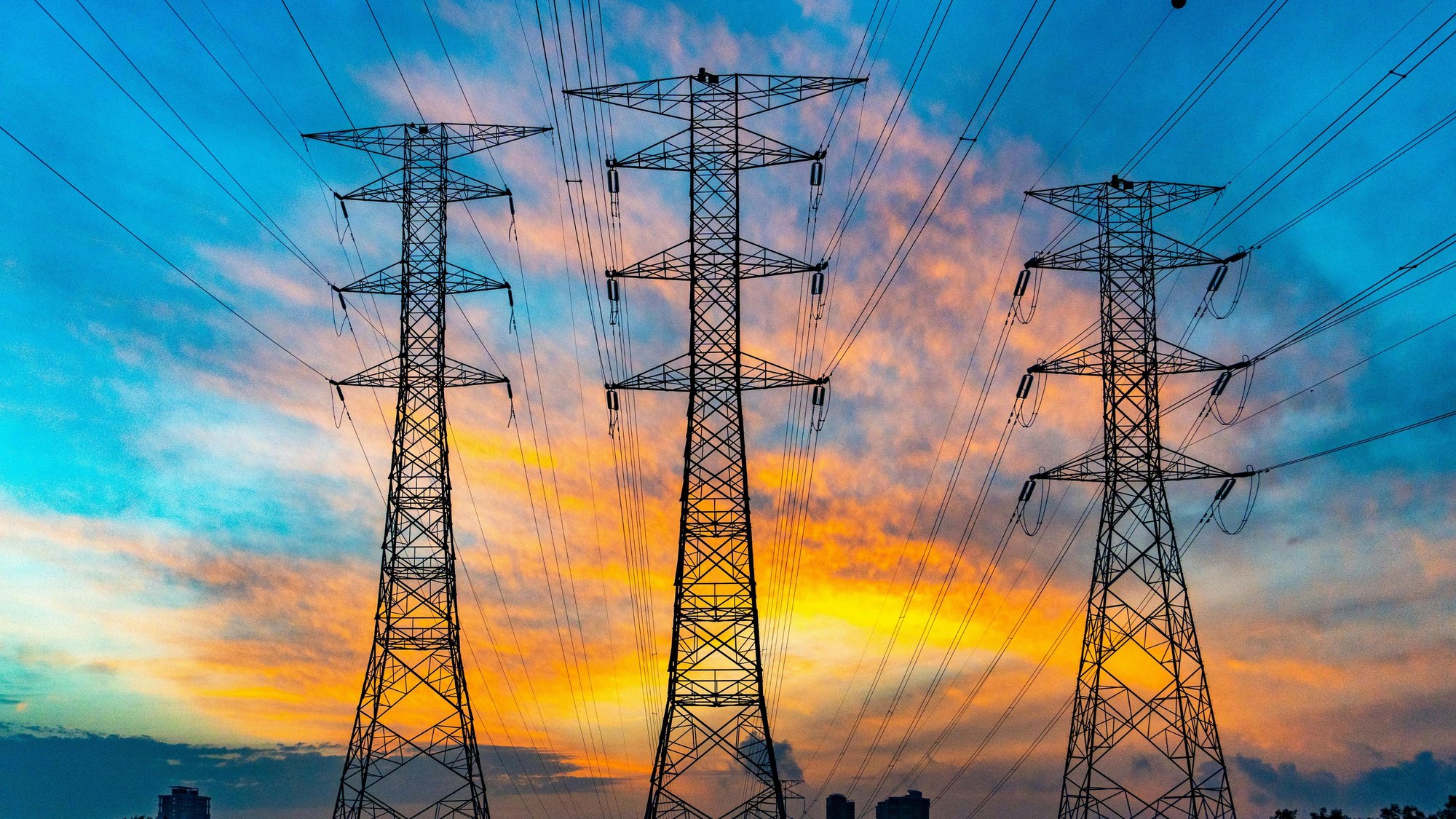 High-voltage transmission towers and power lines silhouetted against an orange sunset