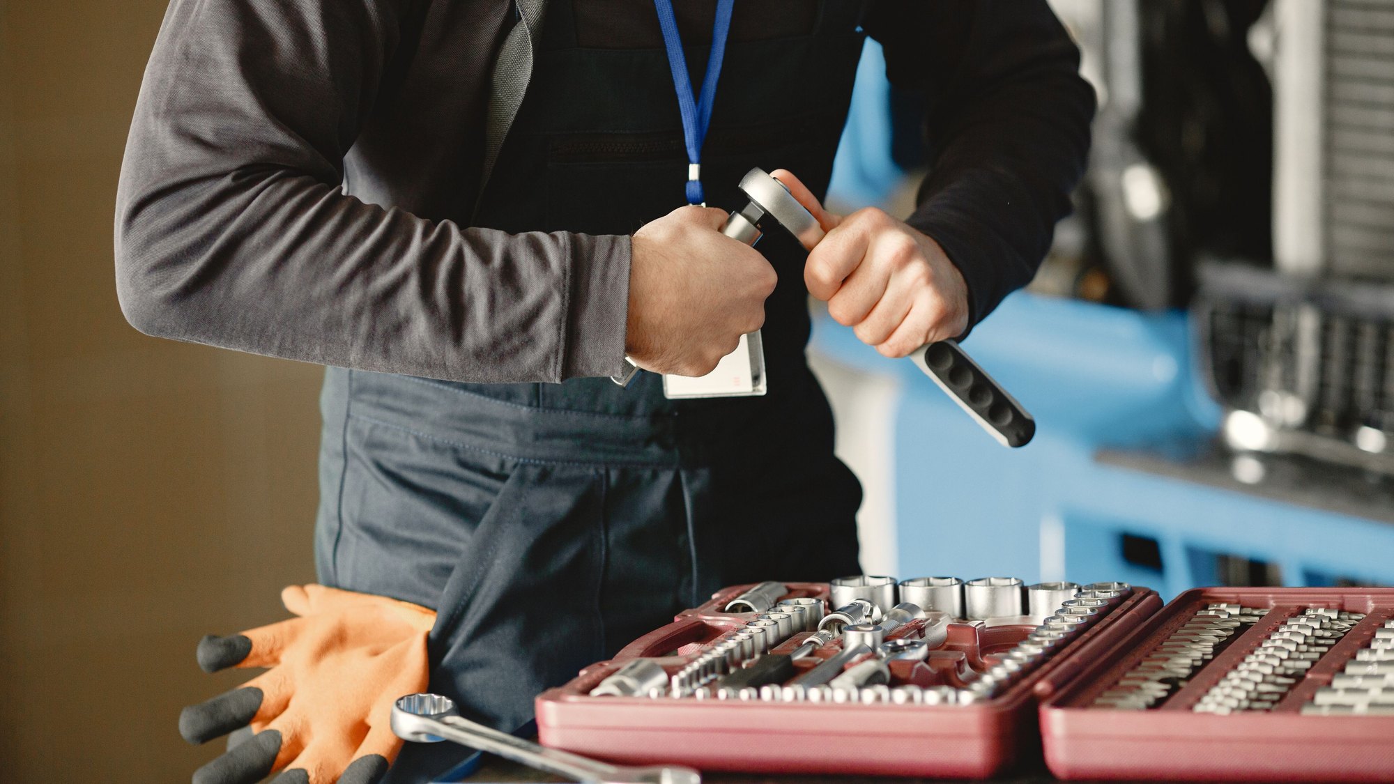 A tradesperson in a work apron lifting a tool from a red socket set