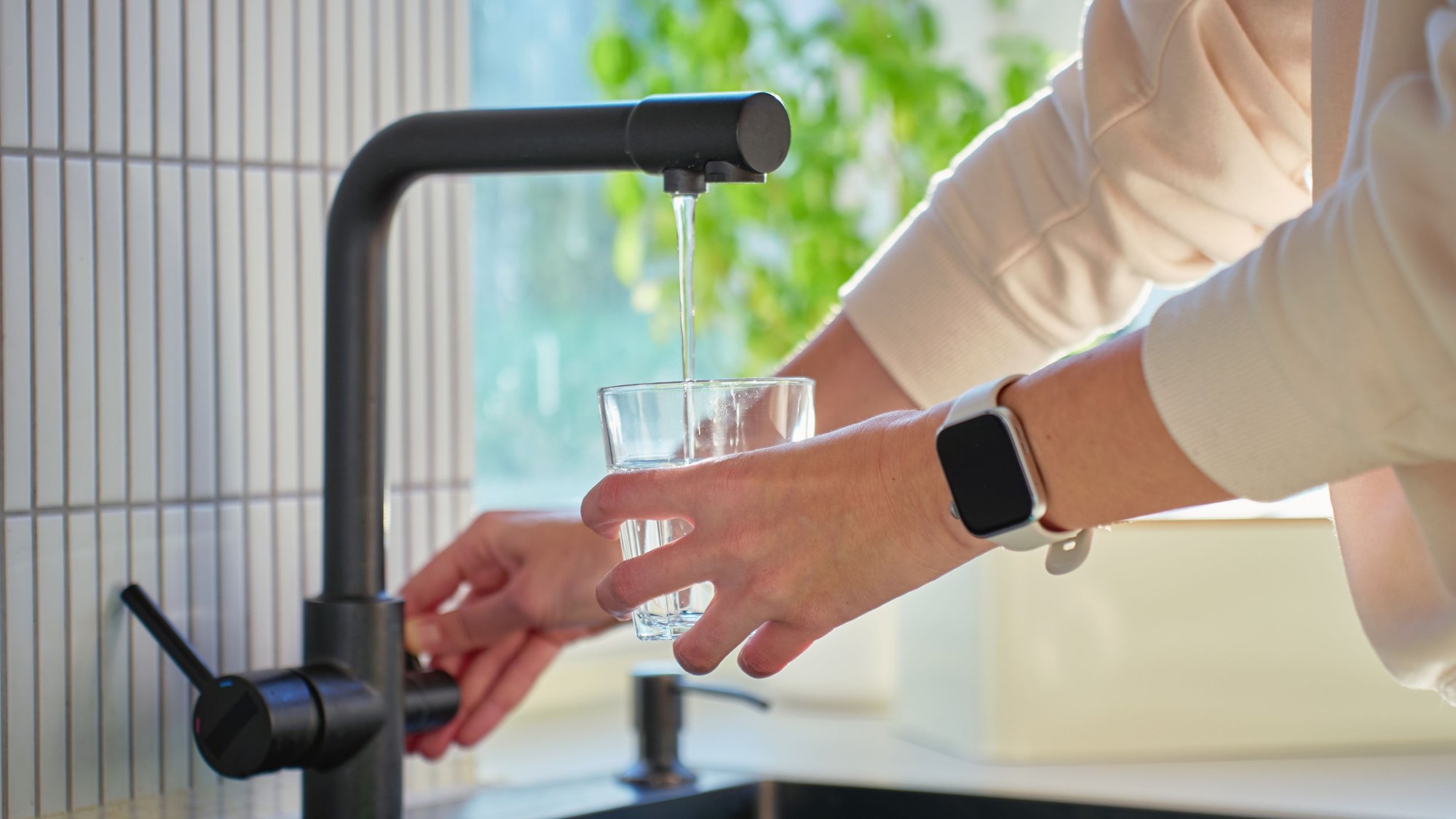 Hands filling a glass of water from a kitchen tap