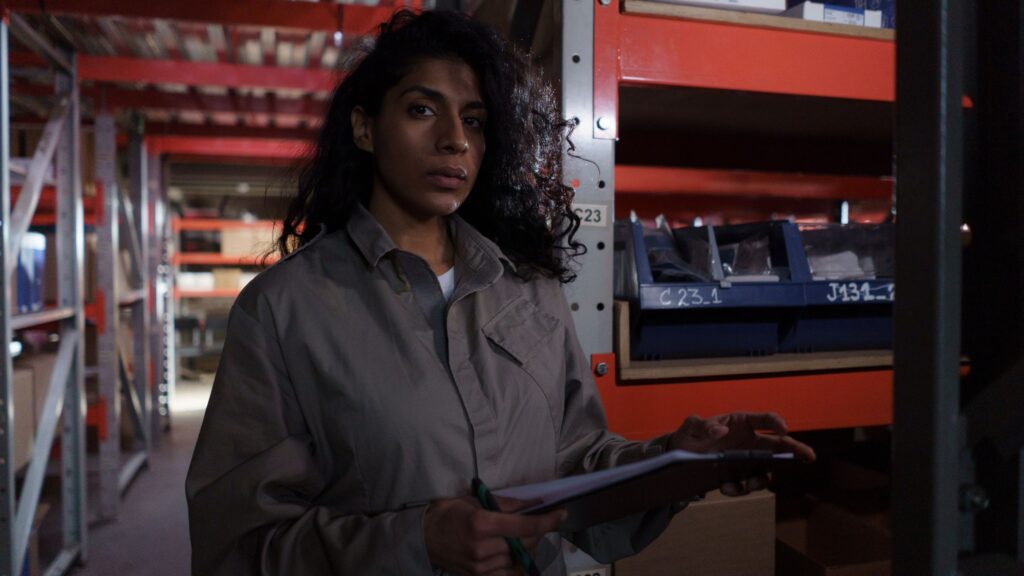 A worker in uniform holding a clipboard beside racking in a warehouse aisle
