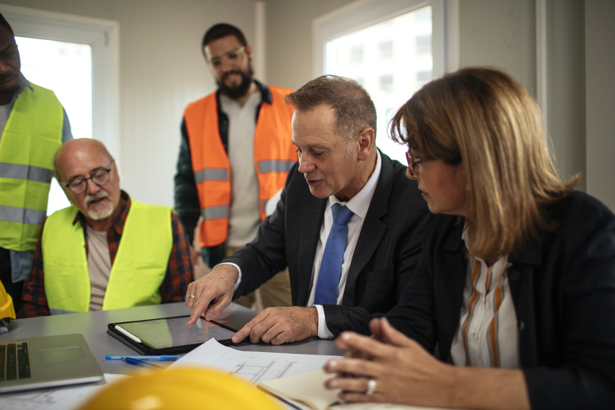A manager walking colleagues and site workers in hi-vis vests through plans on a tablet