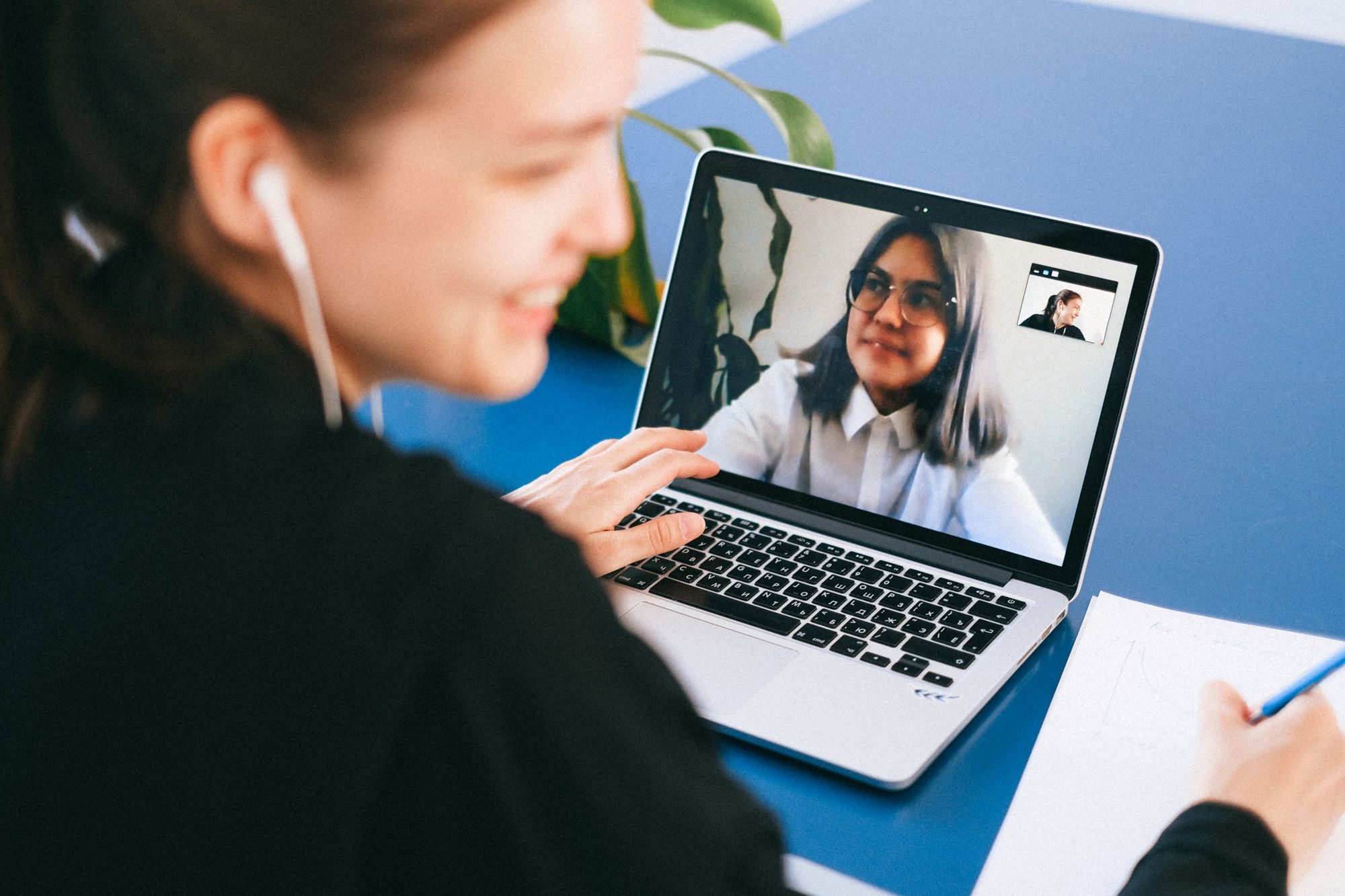 A recruiter smiling and taking notes on a video call with a candidate